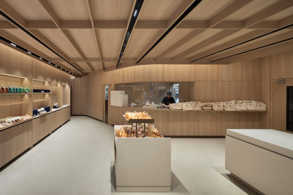 Custom architectural millwork and feature wood ceiling installed throughout a modern Paris Baguette commercial bakery interior.