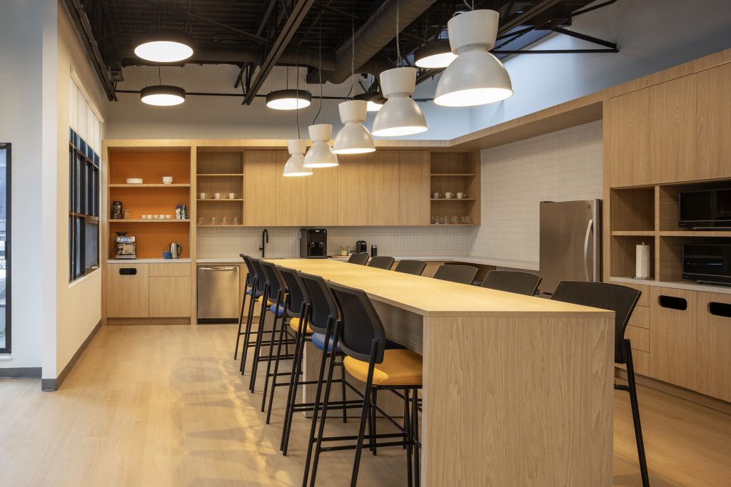 High-end corporate office breakroom featuring custom architectural millwork, commercial wood cabinetry, oversized collaboration island, integrated storage, and premium workplace interior finishes by Boreal Architectural.