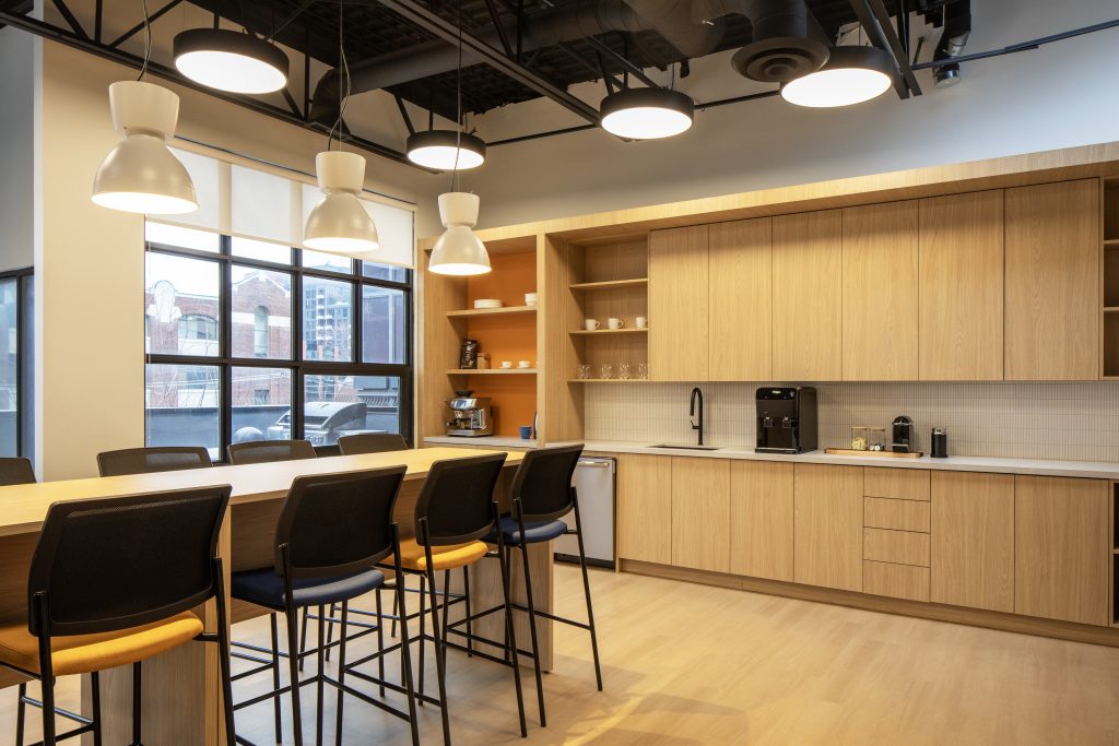 Custom architectural millwork and premium wood finishes in a modern Toronto corporate office featuring commercial kitchenette cabinetry, integrated storage, collaborative island, and contemporary workplace interior by Boreal Architectural.